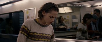 Movie still from “Personal Shopper” (2016), directed by Olivier Assayas – A woman in a gray and yellow sweater looking down; Medium shot, Over the shoulder angle