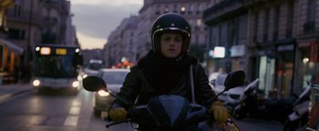 Movie still from “Personal Shopper” (2016), directed by Olivier Assayas – A person riding a motorcycle down a busy street; Medium shot, Over the shoulder angle