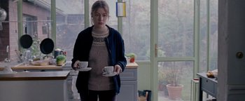 Movie still from “Personal Shopper” (2016), directed by Olivier Assayas – A woman standing in a kitchen holding two white cups; Medium shot, Over the shoulder angle