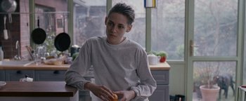 Movie still from “Personal Shopper” (2016), directed by Olivier Assayas – A person holding an orange in a kitchen; Medium shot, Over the shoulder angle