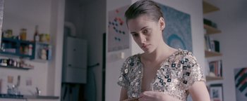 Movie still from “Personal Shopper” (2016), directed by Olivier Assayas – A woman in a silver dress looking at her phone; Medium shot, Over the shoulder angle