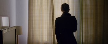 Movie still from “Personal Shopper” (2016), directed by Olivier Assayas – A woman standing in front of a window looking out; Medium shot, Over the shoulder angle