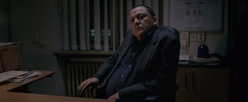 Movie still from “Personal Shopper” (2016), directed by Olivier Assayas – A man sitting at a table in a room; Medium shot, Low angle