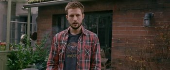 Movie still from “Personal Shopper” (2016), directed by Olivier Assayas – A man standing in front of a brick building; Medium shot, Over the shoulder angle