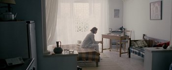 Movie still from “Personal Shopper” (2016), directed by Olivier Assayas – A person sitting on a bed in a room; Wide shot, High angle