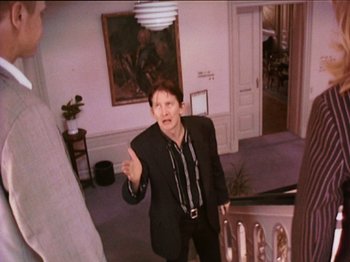 Movie still from “The Celebration” (1998), directed by Thomas Vinterberg – A man in a suit and tie standing next to a staircase; Medium shot, High angle