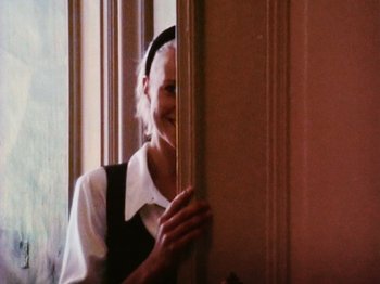 Movie still from “The Celebration” (1998), directed by Thomas Vinterberg – An older woman standing in front of a window; Close Up shot, Over the shoulder angle