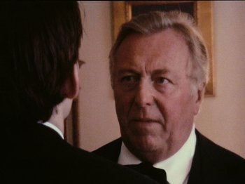 Movie still from “The Celebration” (1998), directed by Thomas Vinterberg – An older man wearing a suit and tie looking at a younger man; Close Up shot, Over the shoulder angle