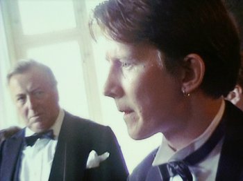 Movie still from “The Celebration” (1998), directed by Thomas Vinterberg – A man in a suit and tie standing next to another man in a suit and tie; Close Up shot, Over the shoulder angle