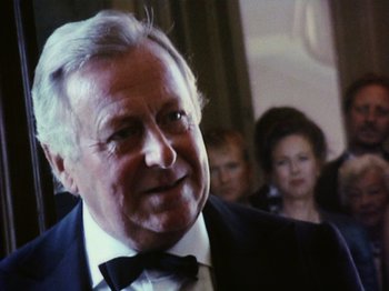 Movie still from “The Celebration” (1998), directed by Thomas Vinterberg – An older man wearing a suit and bow tie in front of a crowd; Close Up shot, Low angle