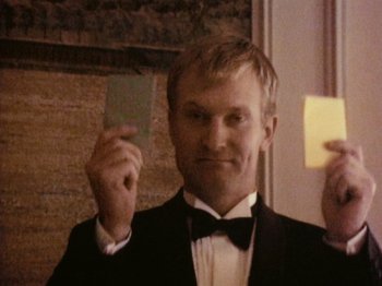 Movie still from “The Celebration” (1998), directed by Thomas Vinterberg – A man in a tuxedo holding up a piece of paper in front of his face; Close Up shot, Over the shoulder angle