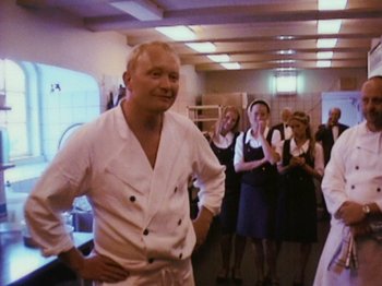 Movie still from “The Celebration” (1998), directed by Thomas Vinterberg – A man standing in front of a group of people; Medium shot, High angle