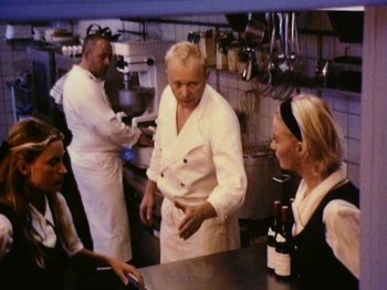 Movie still from “The Celebration” (1998), directed by Thomas Vinterberg – A group of people standing around a restaurant kitchen; Medium shot, High angle