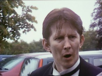 Movie still from “The Celebration” (1998), directed by Thomas Vinterberg – A man in a suit and tie standing next to a car; Close Up shot, Low angle
