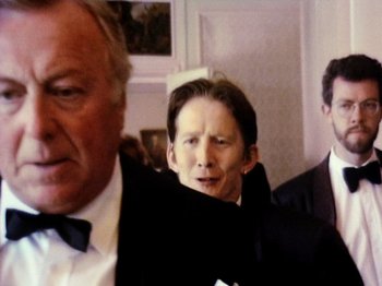 Movie still from “The Celebration” (1998), directed by Thomas Vinterberg – A man in a suit and tie standing next to two other men; Close Up shot, Over the shoulder angle