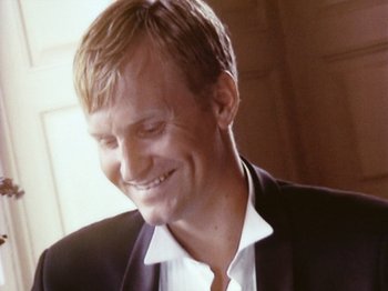 Movie still from “The Celebration” (1998), directed by Thomas Vinterberg – A person wearing a suit and smiling; Close Up shot, Low angle