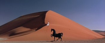 Movie still from “The Cell” (2000), directed by Tarsem Singh – A man standing on top of a sand dune next to a horse; Extreme Wide shot, Low angle