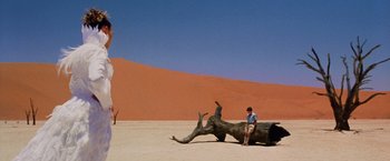 Movie still from “The Cell” (2000), directed by Tarsem Singh – A man sitting on a tree trunk in the desert; Extreme Wide shot, Low angle