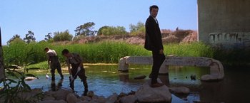 Movie still from “The Cell” (2000), directed by Tarsem Singh – A man in a suit standing on a rock by a river; Wide shot, Low angle