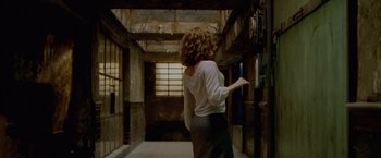 Movie still from “The Cell” (2000), directed by Tarsem Singh – A woman in white shirt and black skirt walking down a hall way; Medium shot, Low angle
