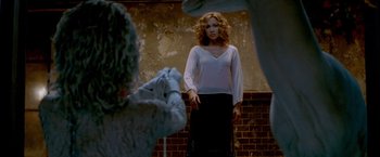 Movie still from “The Cell” (2000), directed by Tarsem Singh – A woman standing in front of a brick wall while a photographer takes a picture of her; Medium shot, Over the shoulder angle