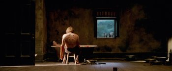 Movie still from “The Cell” (2000), directed by Tarsem Singh – A man sitting in front of a table with a cup on it; Wide shot, High angle