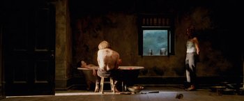 Movie still from “The Cell” (2000), directed by Tarsem Singh – A man sitting at a table in front of a tub; Wide shot, Overhead angle