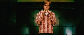 Movie still from “The Cell” (2000), directed by Tarsem Singh – A young boy holding a piece of paper in front of a green wall; Medium shot, Overhead angle