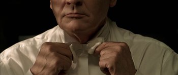 Movie still from “The Chorus” (2004), directed by Christophe Barratier – An older man adjusting his bow tie in front of a black background; Extreme Close Up shot, Low angle