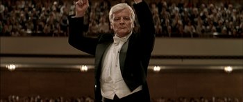Movie still from “The Chorus” (2004), directed by Christophe Barratier – An older man in a tuxedo raises his hands; Medium shot, Low angle