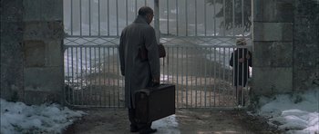 Movie still from “The Chorus” (2004), directed by Christophe Barratier – A man in a gray coat holding a suit case; Wide shot, Low angle