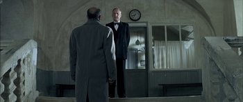 Movie still from “The Chorus” (2004), directed by Christophe Barratier – Two men standing in front of each other in front of a clock; Wide shot, Low angle
