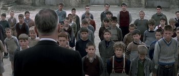 Movie still from “The Chorus” (2004), directed by Christophe Barratier – A group of young men standing next to each other in front of an older man; Wide shot, High angle