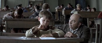 Movie still from “The Chorus” (2004), directed by Christophe Barratier – A man and a boy sitting at a table in a classroom; Medium shot, Over the shoulder angle