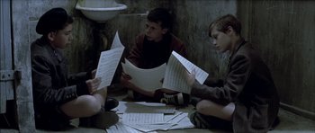 Movie still from “The Chorus” (2004), directed by Christophe Barratier – A group of people sitting on the ground with papers; Medium shot, High angle