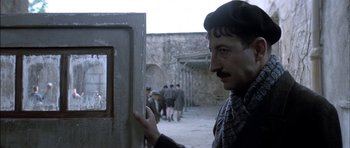 Movie still from “The Chorus” (2004), directed by Christophe Barratier – A man standing in front of a door with a bunch of people in the background; Close Up shot, Over the shoulder angle