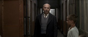 Movie still from “The Chorus” (2004), directed by Christophe Barratier – A man in a suit and tie standing in a hallway; Medium shot, Low angle