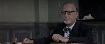 Movie still from “The Chorus” (2004), directed by Christophe Barratier – An older man sitting at a table wearing a bow tie; Close Up shot, Over the shoulder angle