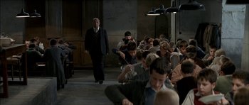 Movie still from “The Chorus” (2004), directed by Christophe Barratier – A group of people sitting in a room with a man in a suit; Wide shot, High angle