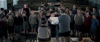 Movie still from “The Chorus” (2004), directed by Christophe Barratier – A group of young people standing in front of an older man; Medium shot, High angle