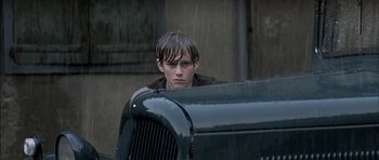 Movie still from “The Chorus” (2004), directed by Christophe Barratier – A young man leaning on the hood of an antique car; Close Up shot, Over the shoulder angle
