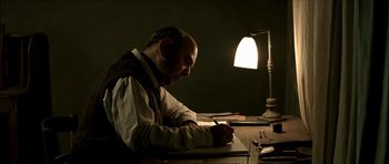 Movie still from “The Chorus” (2004), directed by Christophe Barratier – A man sitting at a desk writing on a piece of paper; Medium shot, Low angle