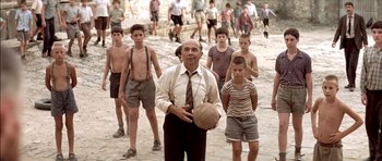 Movie still from “The Chorus” (2004), directed by Christophe Barratier – An older man holding a ball in front of a group of young boys; Wide shot, High angle