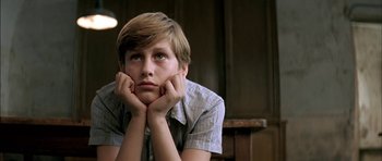 Movie still from “The Chorus” (2004), directed by Christophe Barratier – A young boy sitting in front of a wooden table; Close Up shot, Low angle
