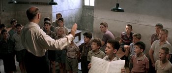 Movie still from “The Chorus” (2004), directed by Christophe Barratier – A group of young boys singing in a room; Medium shot, High angle