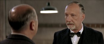 Movie still from “The Chorus” (2004), directed by Christophe Barratier – A man in a suit and a bow tie talking to another man in a suit and a bow tie; Close Up shot, Over the shoulder angle