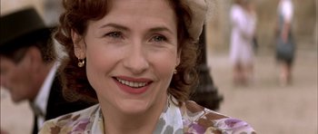 Movie still from “The Chorus” (2004), directed by Christophe Barratier – An older woman wearing a hat and smiling for the camera; Close Up shot, Over the shoulder angle