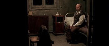 Movie still from “The Chorus” (2004), directed by Christophe Barratier – A man sitting on a bed next to a woman in a room; Wide shot, High angle