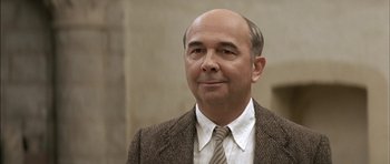 Movie still from “The Chorus” (2004), directed by Christophe Barratier – A bald man in a suit and tie looking to his left; Close Up shot, Low angle