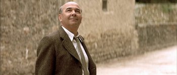 Movie still from “The Chorus” (2004), directed by Christophe Barratier – A man wearing a suit and tie standing in front of a building; Close Up shot, Low angle